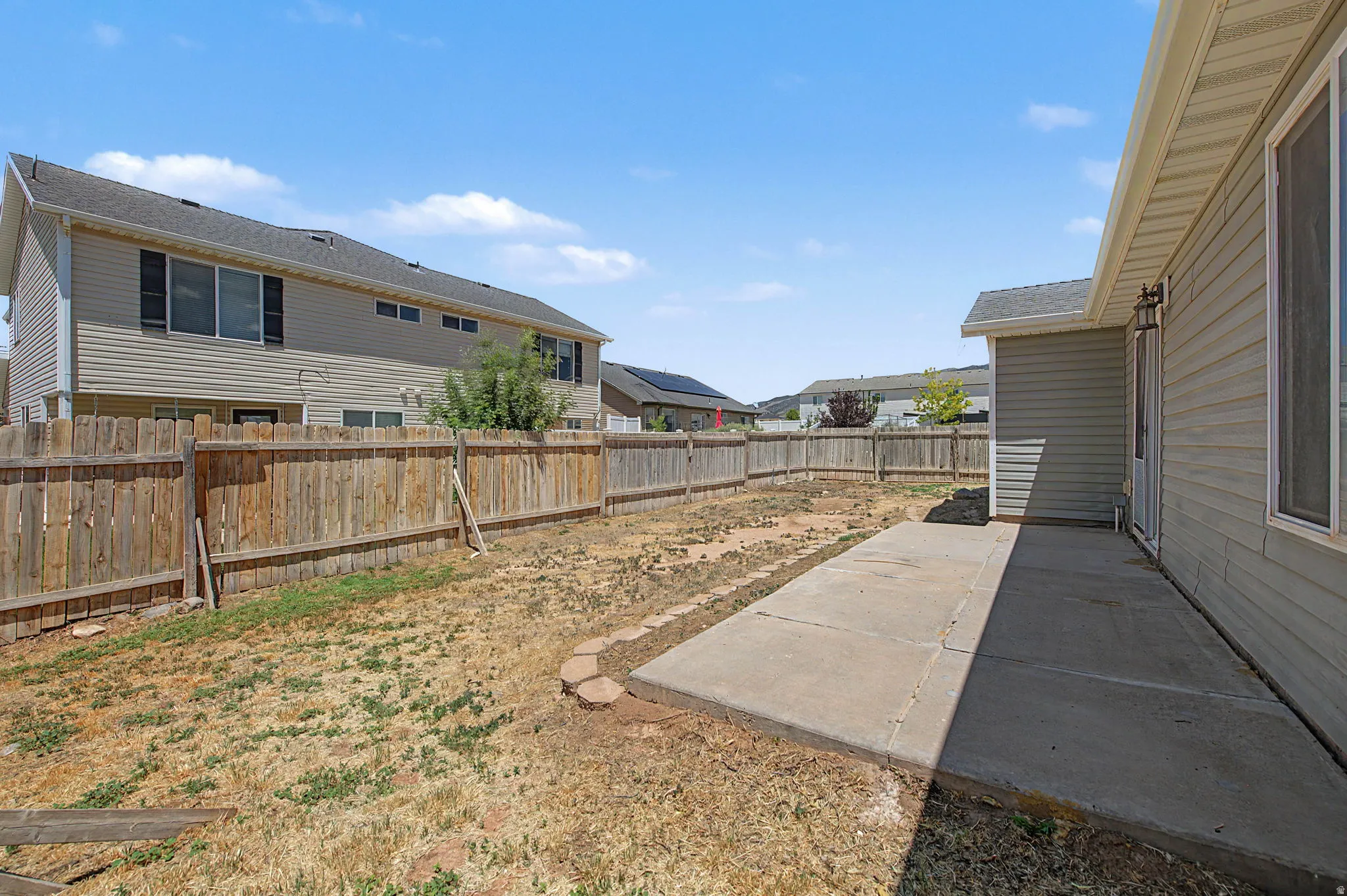 Expansive backyard featuring a concrete patio, wood privacy fencing, and direct access to the home's exterior with horizontal siding