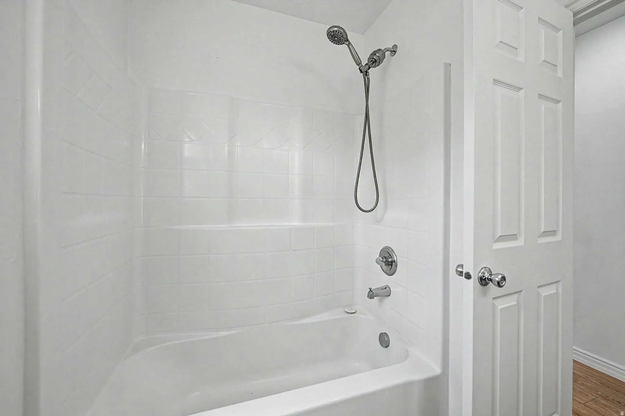 White fiberglass tub and shower combination featuring a brushed nickel showerhead and faucet