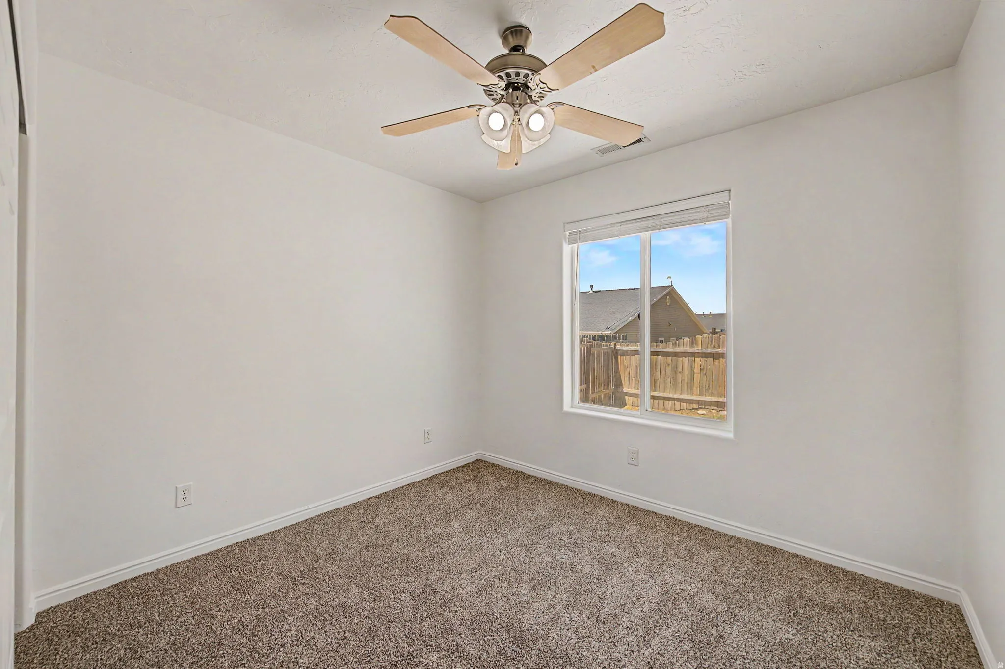 Carpeted room with a ceiling fan featuring light wood-tone blades and a central light fixture