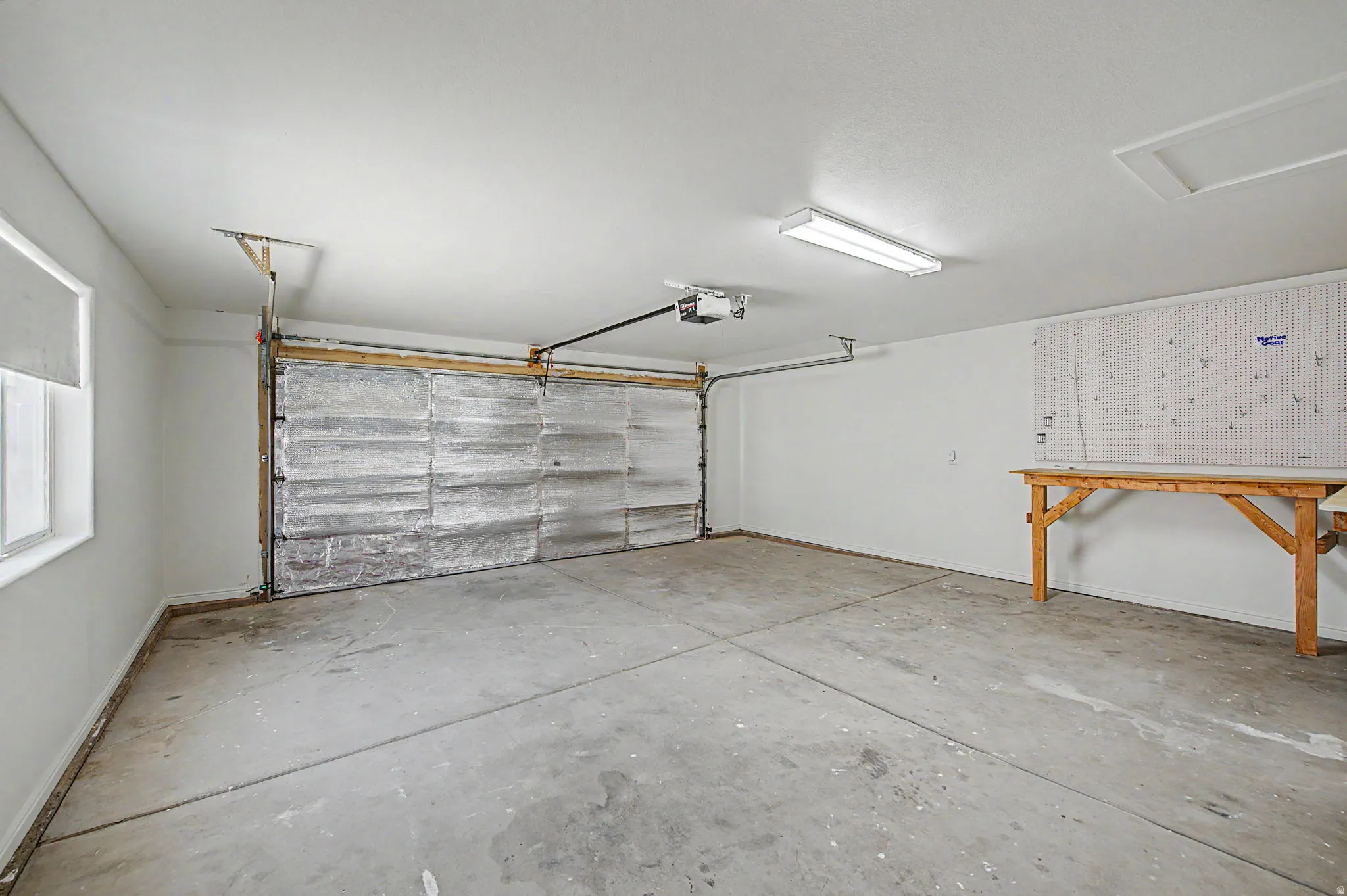Spacious garage featuring a concrete floor, white painted walls, and a large window with roller shades