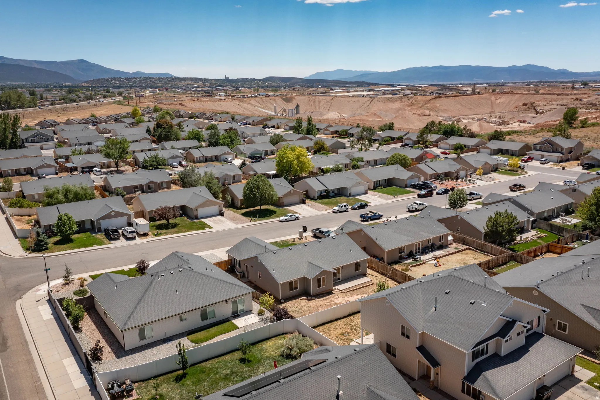 Residential neighborhood featuring varied single-family homes with gray shingle roofs, paved streets, and mountainous terrain in the background