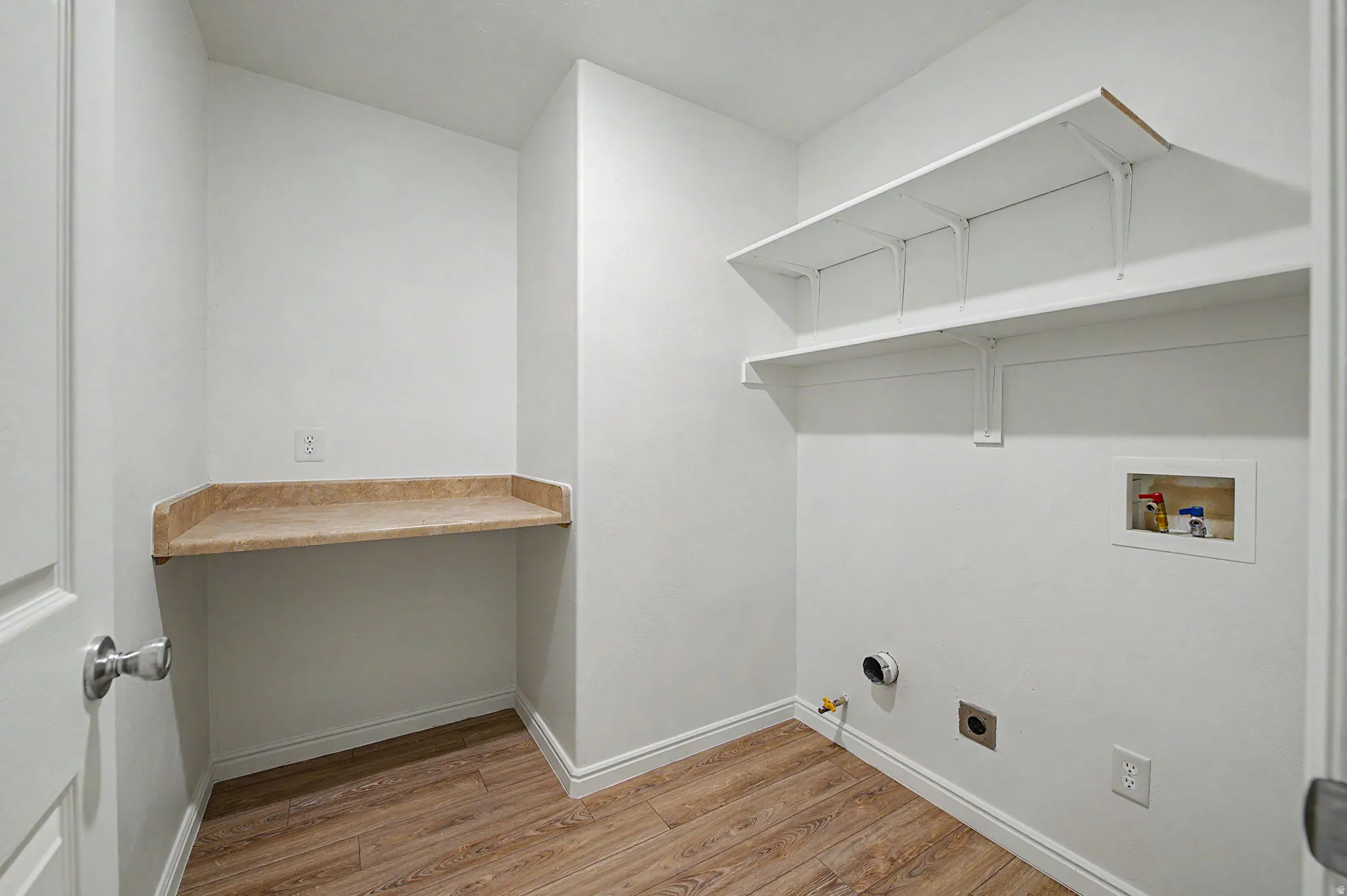 Dedicated laundry space featuring wood-finish flooring, a built-in counter surface, and two storage shelves