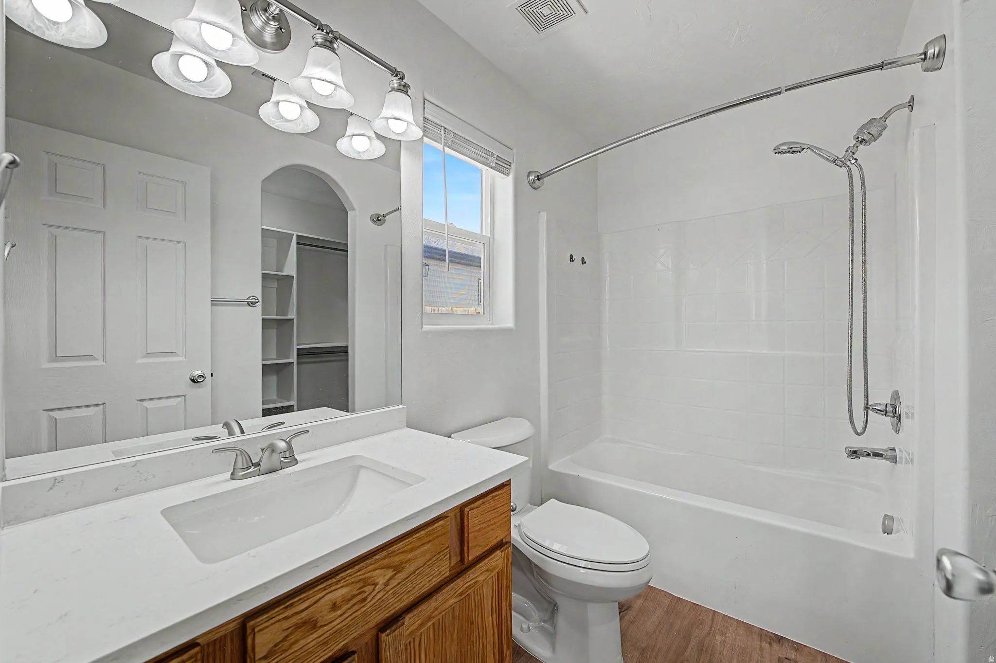 Bathroom featuring a wood-finish vanity with a white countertop and integrated sink, brushed nickel faucet, and overhead vanity lighting