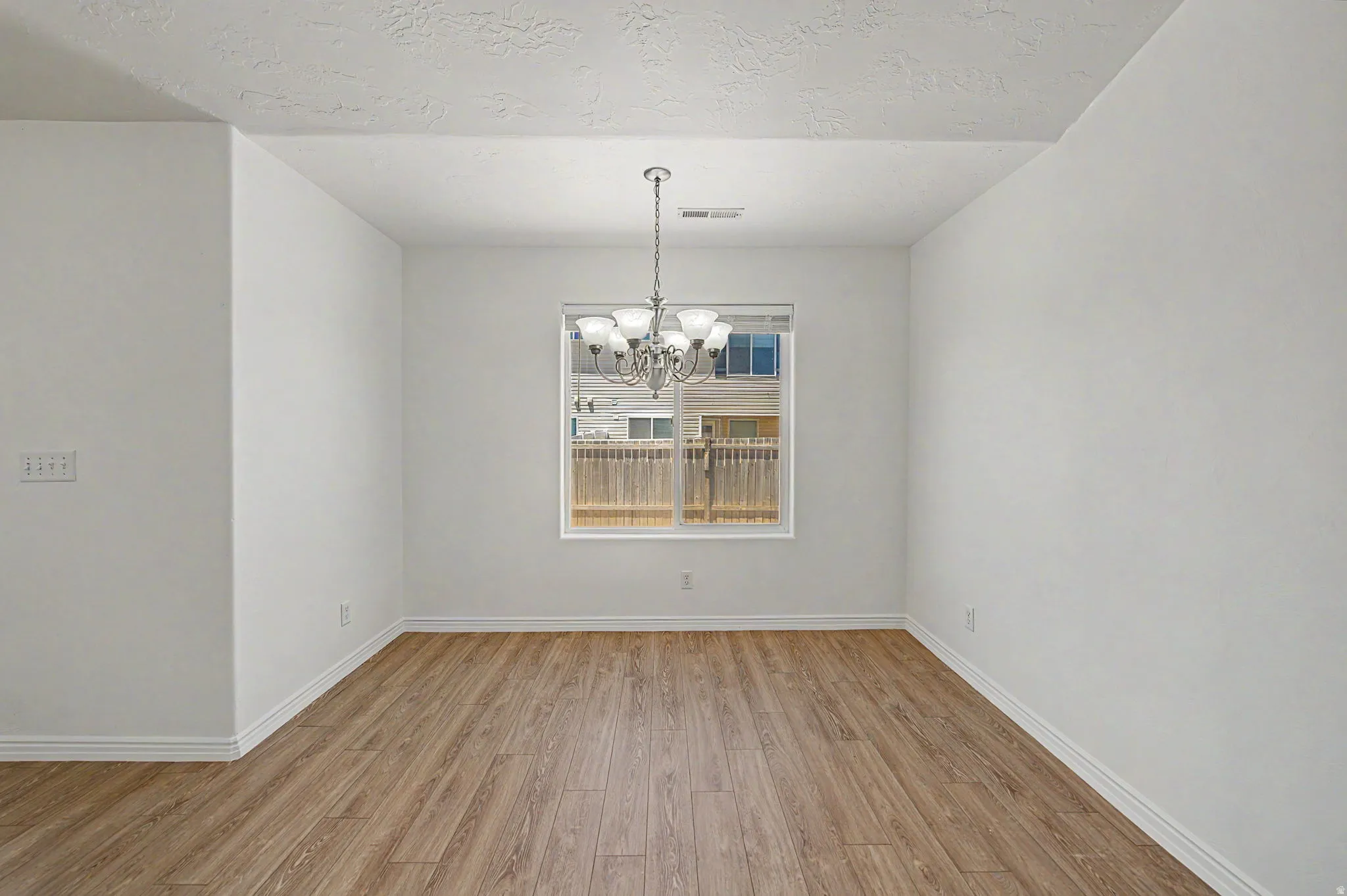 Spacious room featuring wood-finish flooring, white baseboards, and a contemporary chandelier