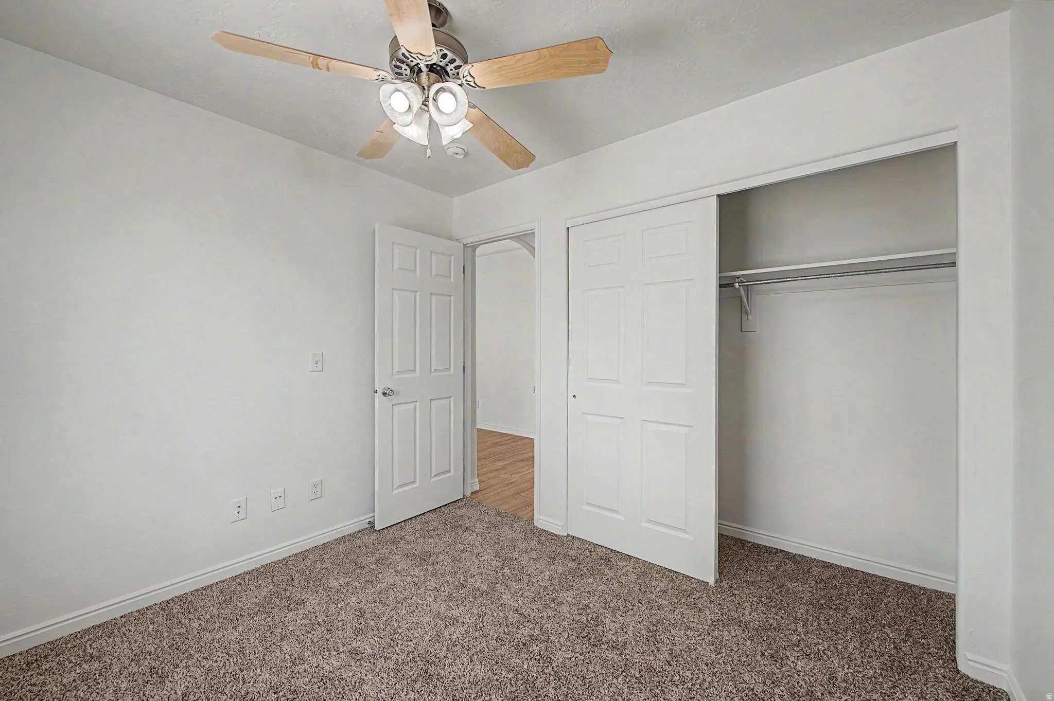 Carpeted room with a ceiling fan, white walls, and white baseboards