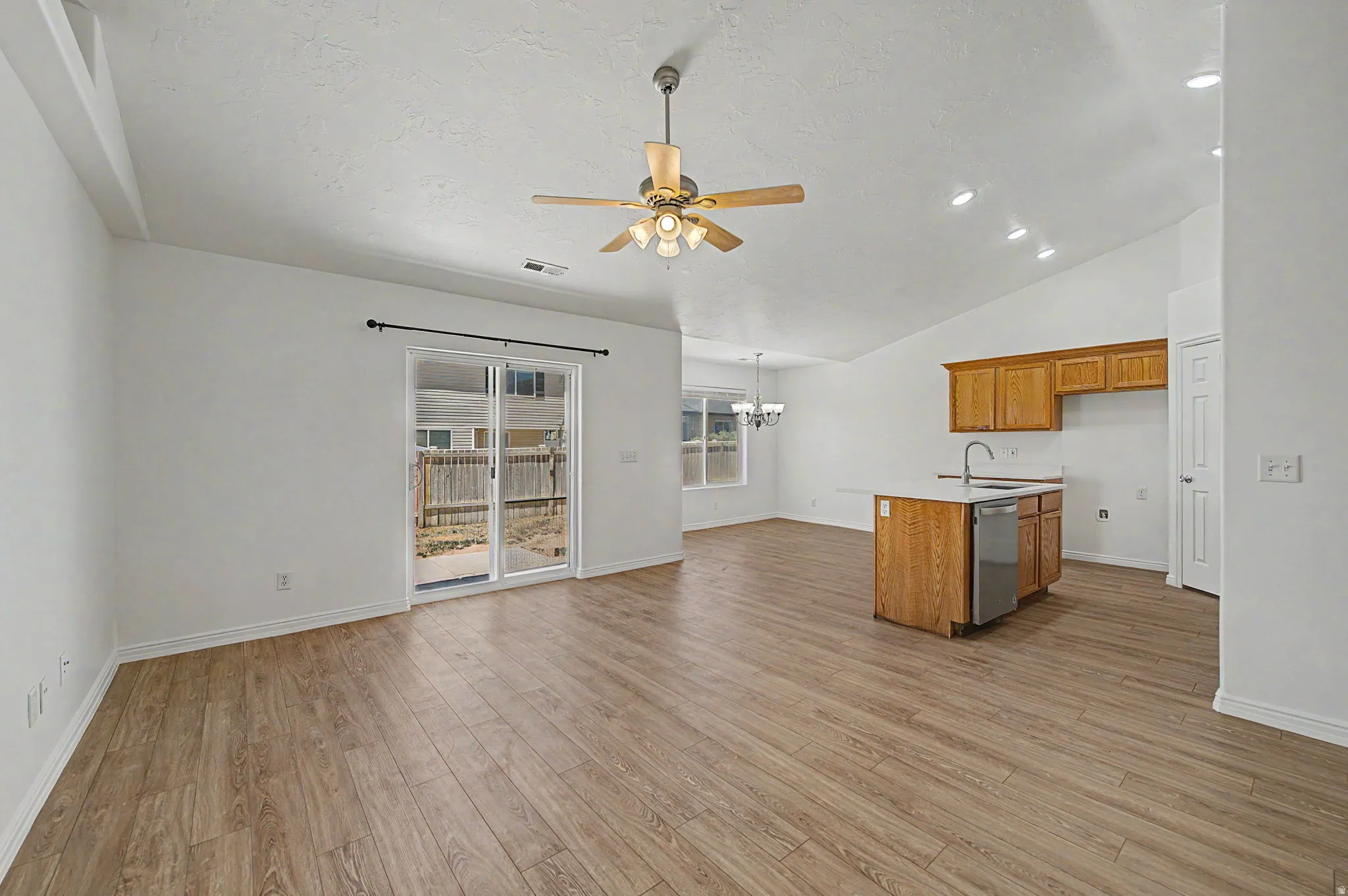 Vaulted ceilings provide vertical dimension to this open-concept space featuring wood-finish flooring, a kitchen island with integrated dishwasher, and a sliding glass door for outdoor access