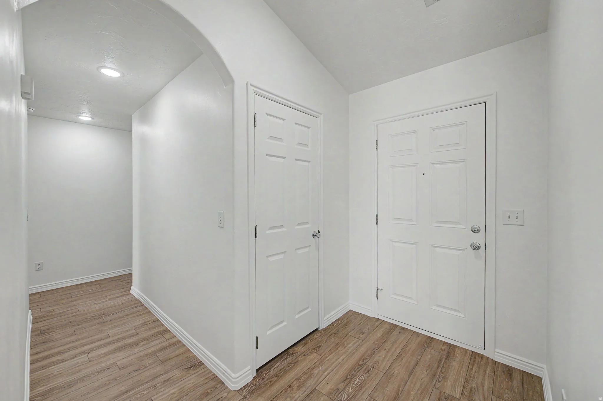 Entryway featuring durable wood-finish flooring, white paneled doors, recessed ceiling lighting, and crisp white baseboards