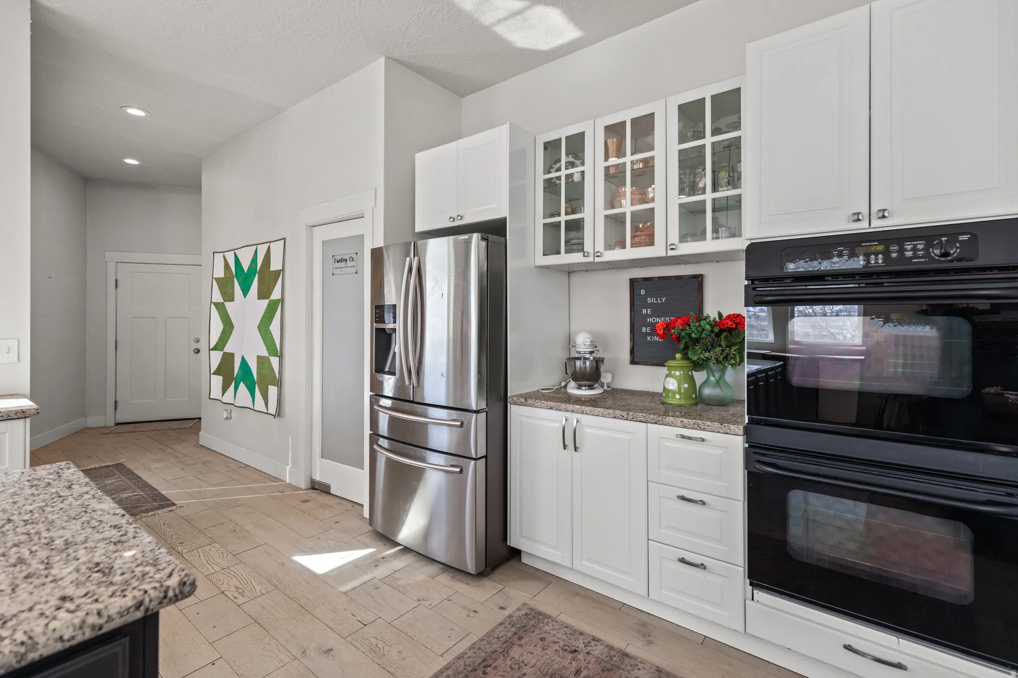 Kitchen featuring white cabinetry, granite countertops, stainless steel refrigerator, black double wall ovens, and wood-finish flooring