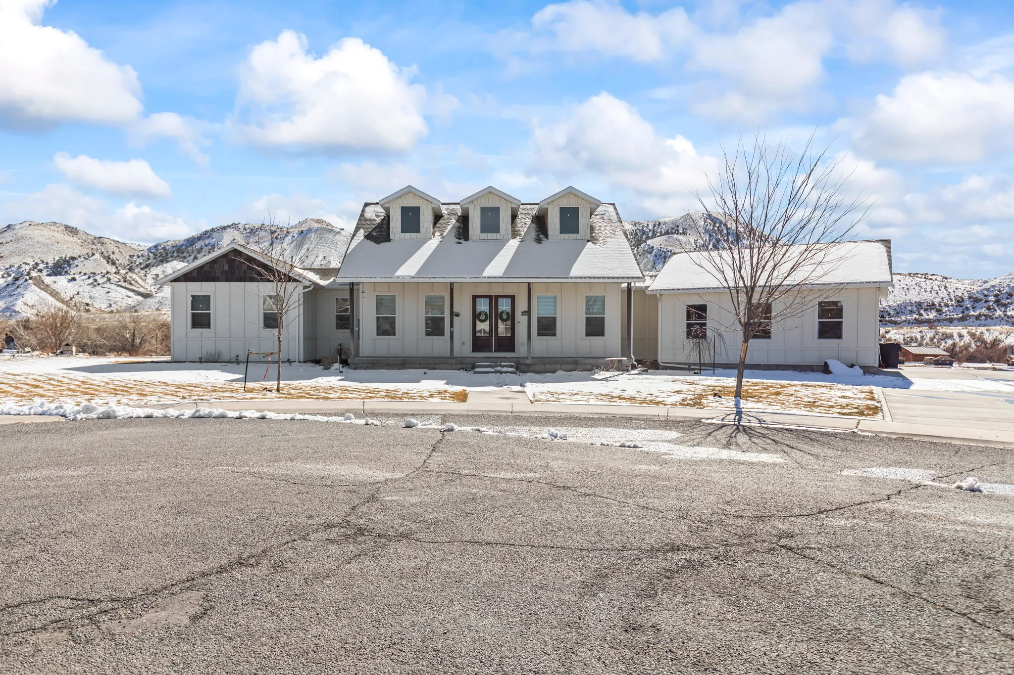 White siding residence featuring multiple dormer windows, a covered front porch, and a dark double entry door