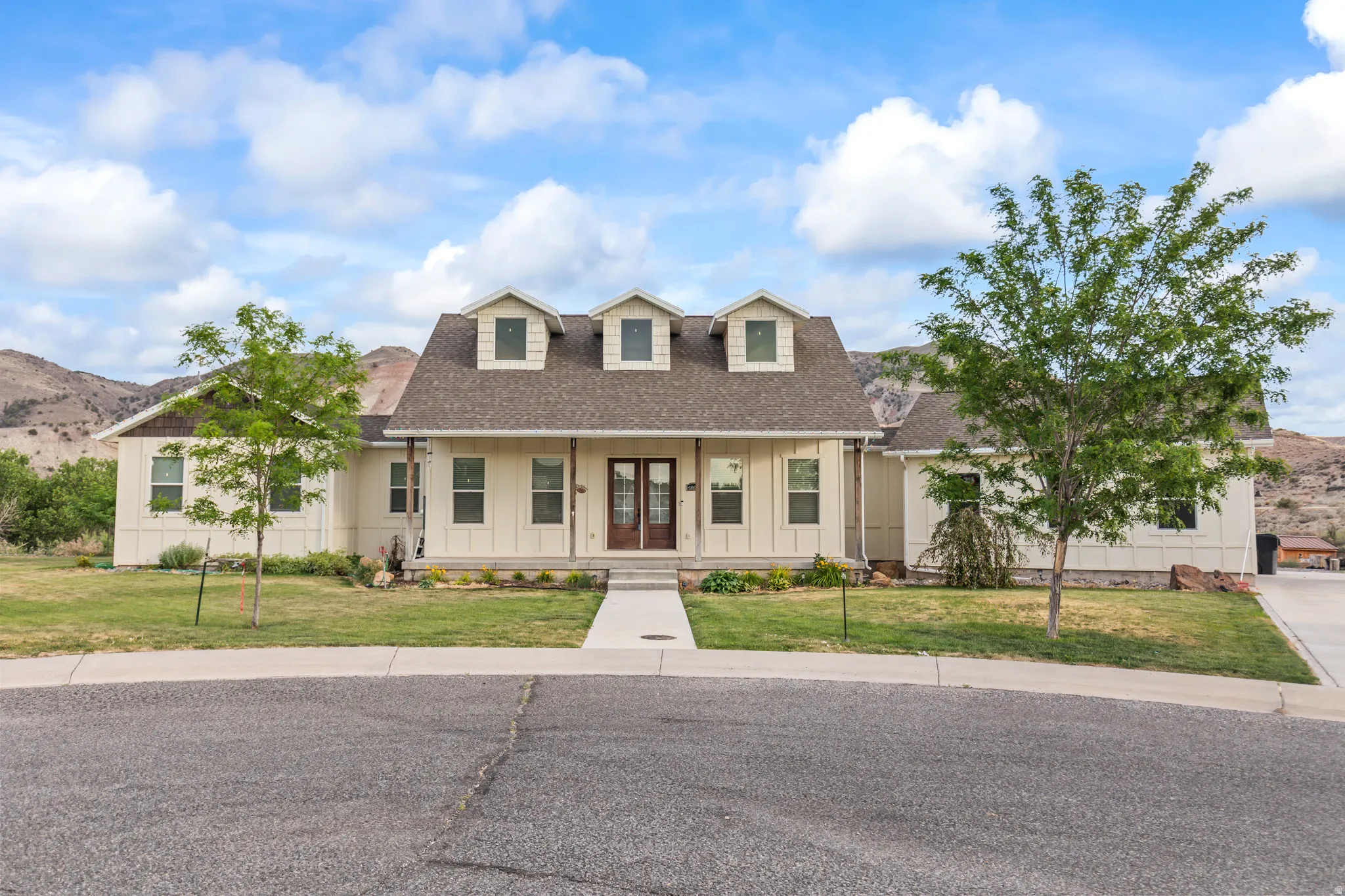 Single-story residence featuring a covered front porch with dark wood double entry doors, dormer windows, and a shingled roof
