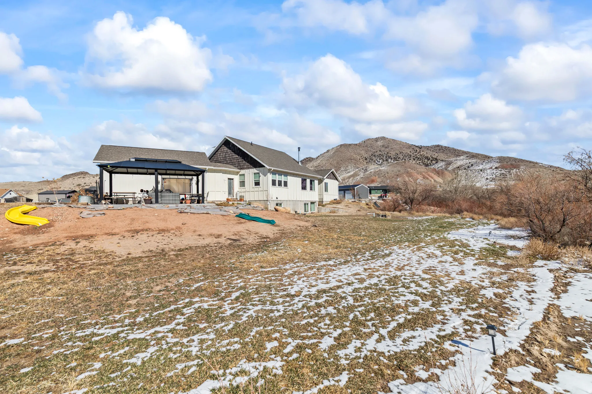 Spacious exterior featuring a covered patio, expansive land, and mountain backdrop