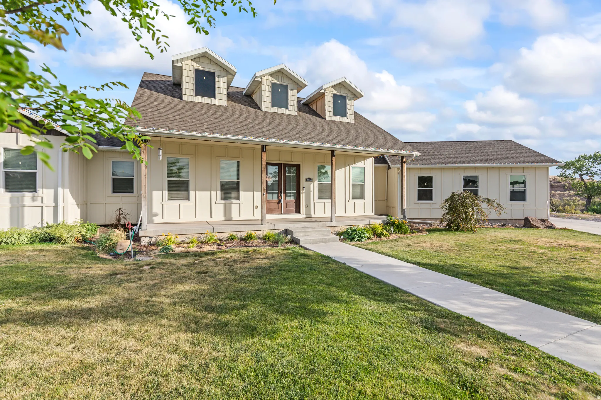 Ranch-style residence featuring a prominent covered porch entryway, board and batten siding, multiple dormer windows, and a dark shingle roof