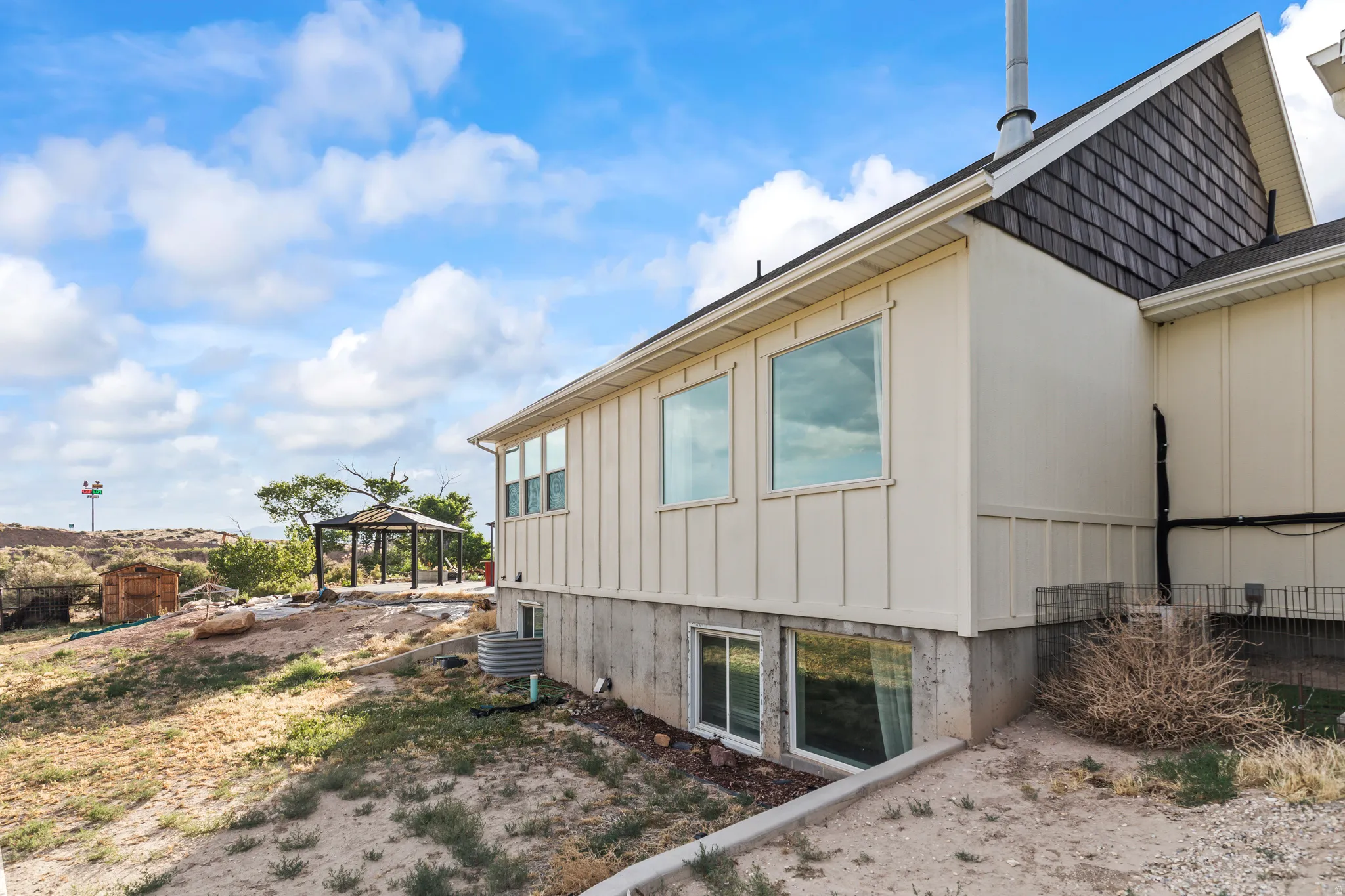 Cream-colored vertical board and batten siding with a concrete foundation and two lower-level egress windows