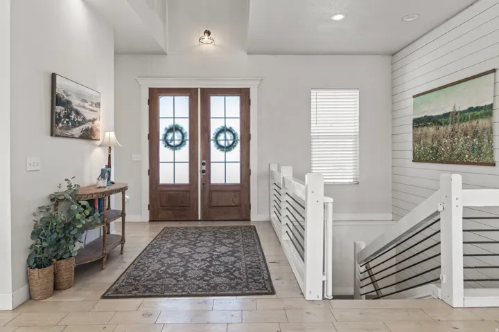 Entryway featuring double wood-finish doors with frosted glass panels, tile flooring, and a contemporary staircase with white newel posts and dark horizontal balusters