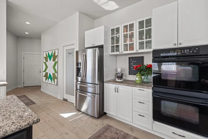 Kitchen featuring white cabinetry, granite countertops, stainless steel refrigerator, black double wall ovens, and wood-finish flooring