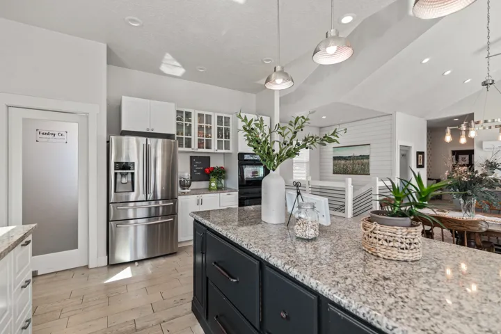 Spacious kitchen featuring a large island with a stone countertop, white cabinetry, integrated stainless steel appliances, and wood-finish flooring