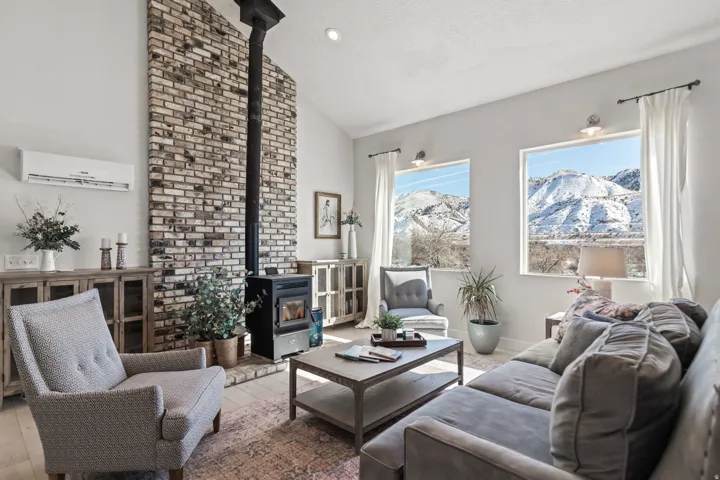 Vaulted ceiling living area featuring a brick accent wall with a wood-burning stove, large windows, and light wood-finish flooring