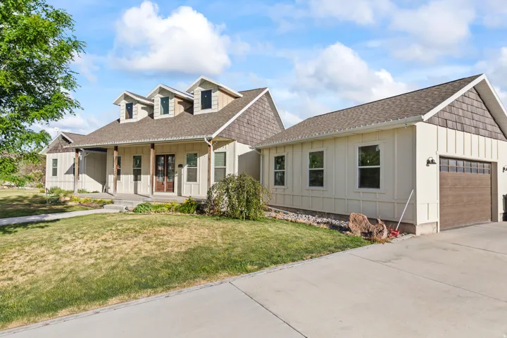 Craftsman-style home featuring a covered front porch with substantial columns, a two-car garage with a wood-finish door, dormer windows, and board and batten siding