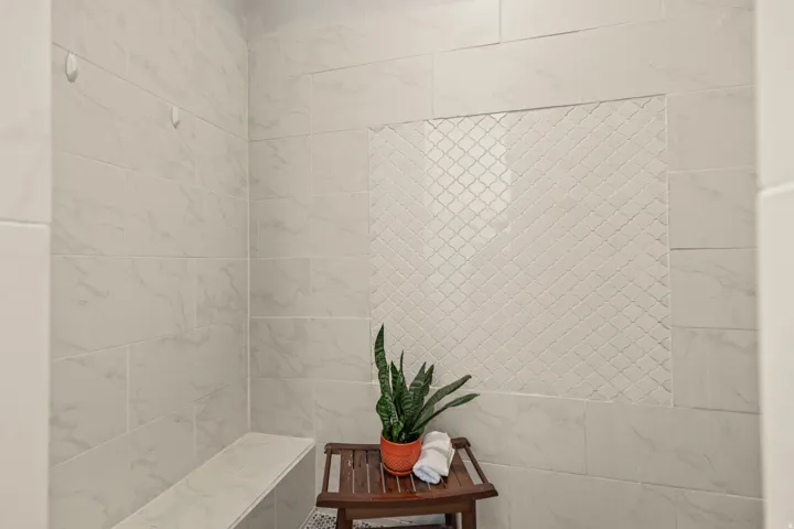 Shower featuring large format white tile with subtle veining, an accent wall of arabesque-patterned tile, and a built-in tiled bench