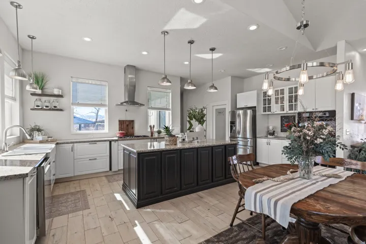 Spacious kitchen featuring a central island with dark cabinetry, light-toned wood-finish flooring, white perimeter cabinetry, stainless steel appliances, and recessed lighting