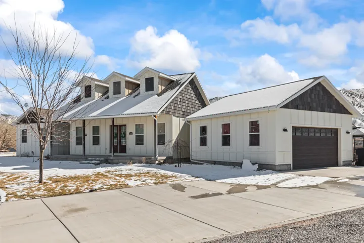 Modern farmhouse exterior featuring board and batten siding, multiple dormer windows, a covered front porch, and a detached two-car garage with a dark wood-finish door