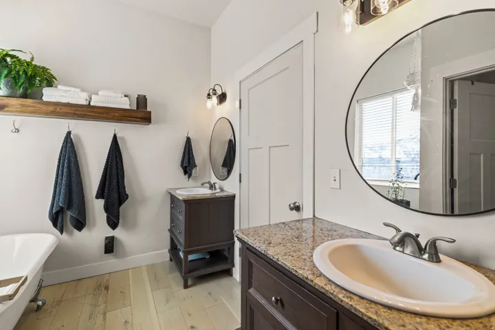Bathroom featuring dual dark wood vanities with granite-style countertops, an oval undermount sink, and brushed nickel hardware