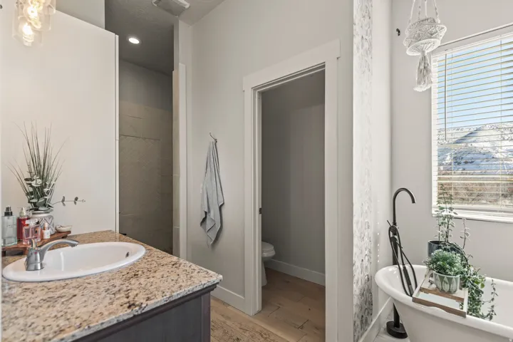 Bathroom featuring a vanity with a light-toned speckled countertop, an undermount sink, a freestanding tub with a matte black faucet, and a separate water closet