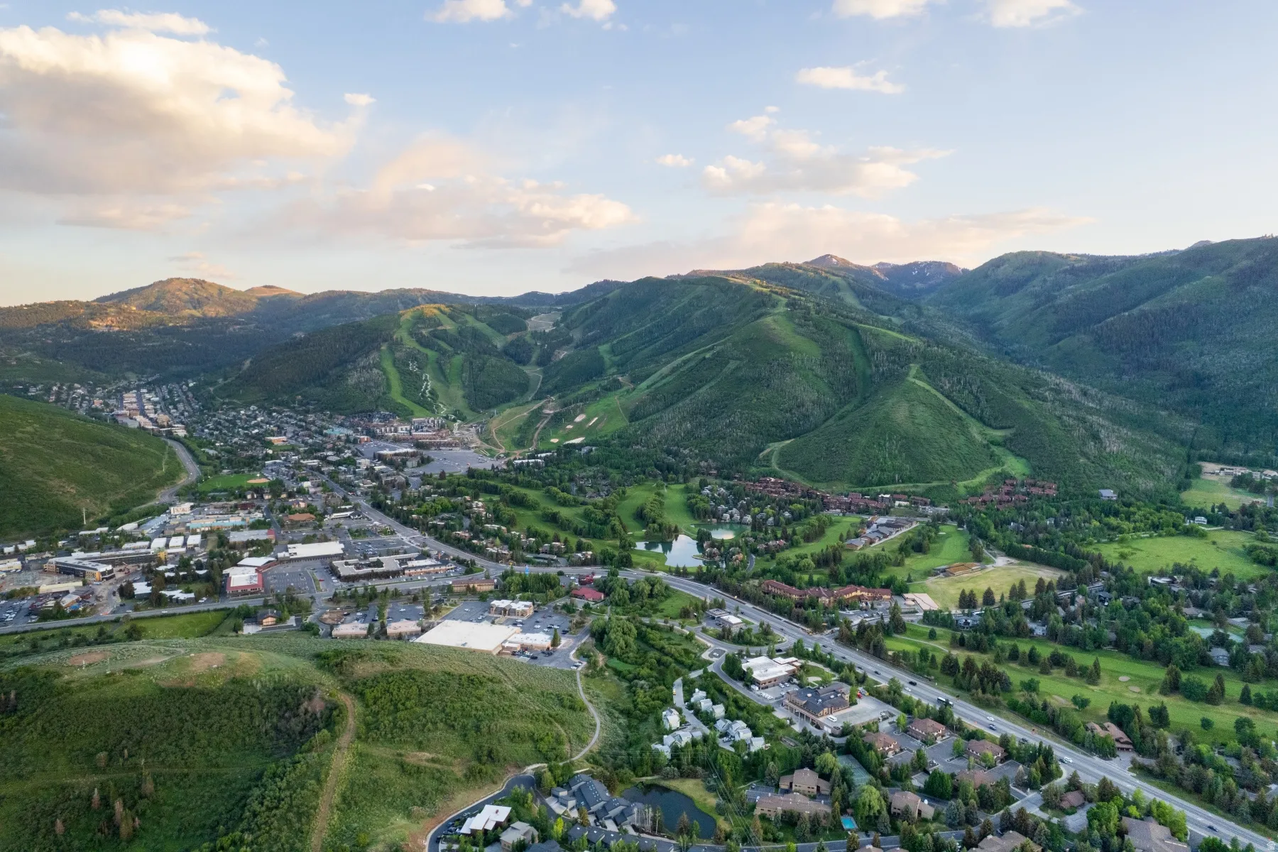 Expansive aerial perspective showcasing a mountainous terrain with lush green slopes and scattered snow patches