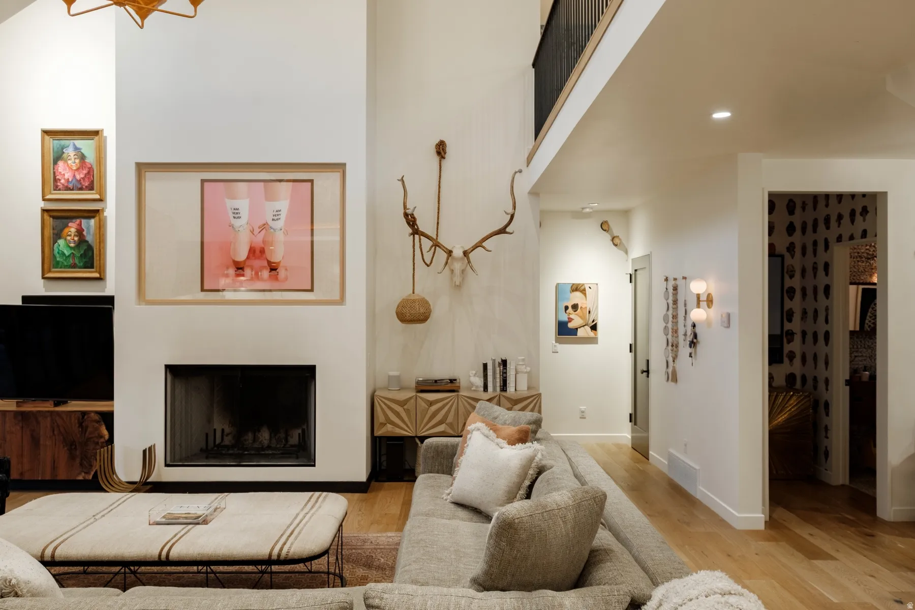 Vaulted ceiling living area featuring a fireplace, wood-finish flooring, a second-story interior balcony, and built-in wall sconces