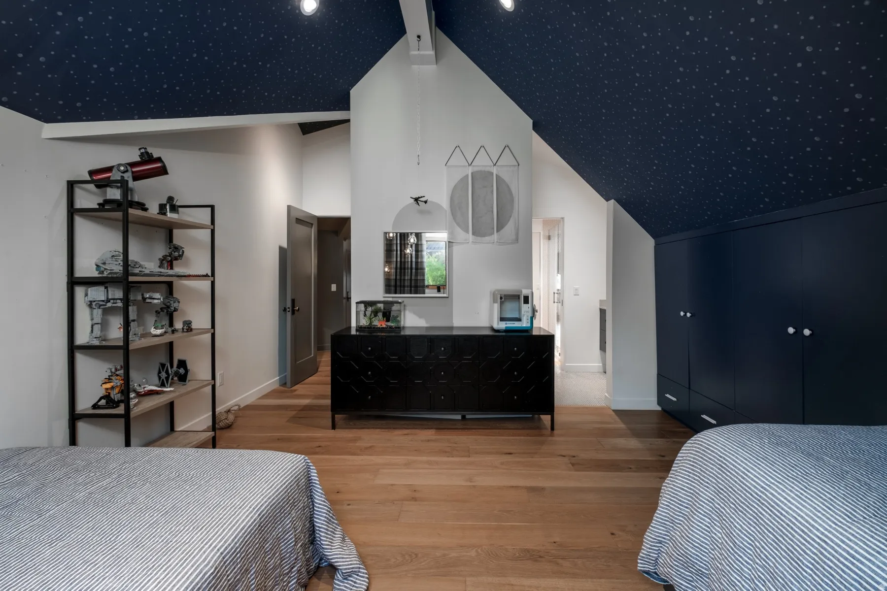 Room featuring a dark blue ceiling with a light-colored pattern, light wood-finish flooring, white walls, and built-in dark blue cabinetry with white knobs