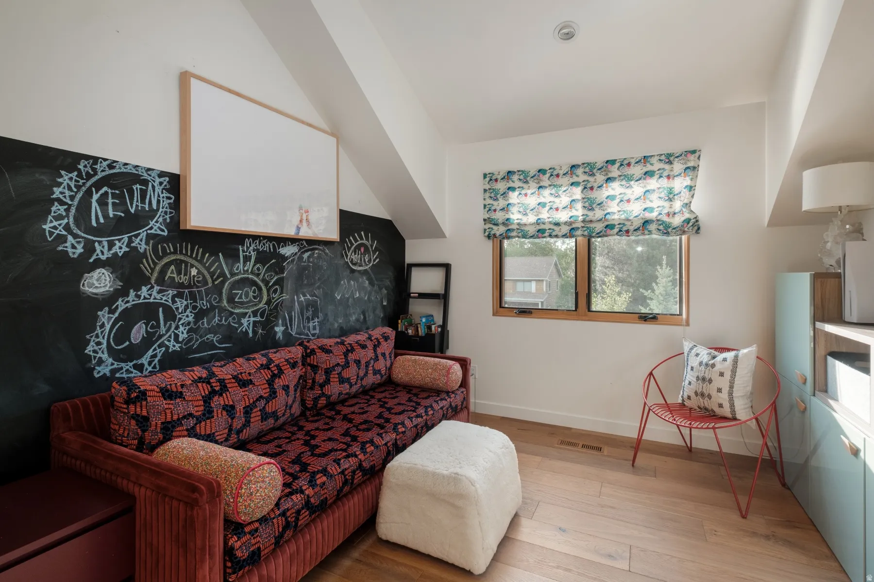 Attic room featuring an angled ceiling, wood-finish flooring, and a large window with a patterned Roman shade