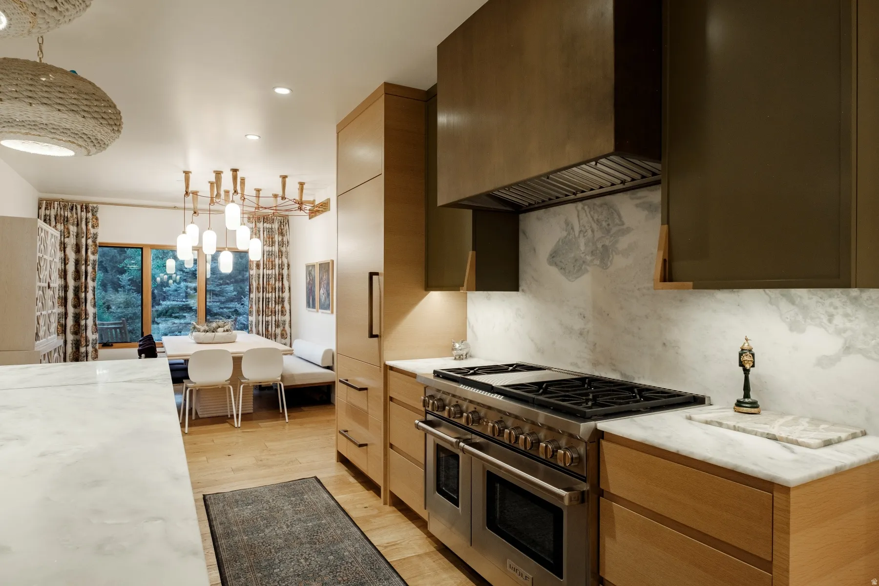 Gourmet kitchen featuring a stainless steel range with double ovens, a stone slab backsplash, and light wood-finish cabinetry