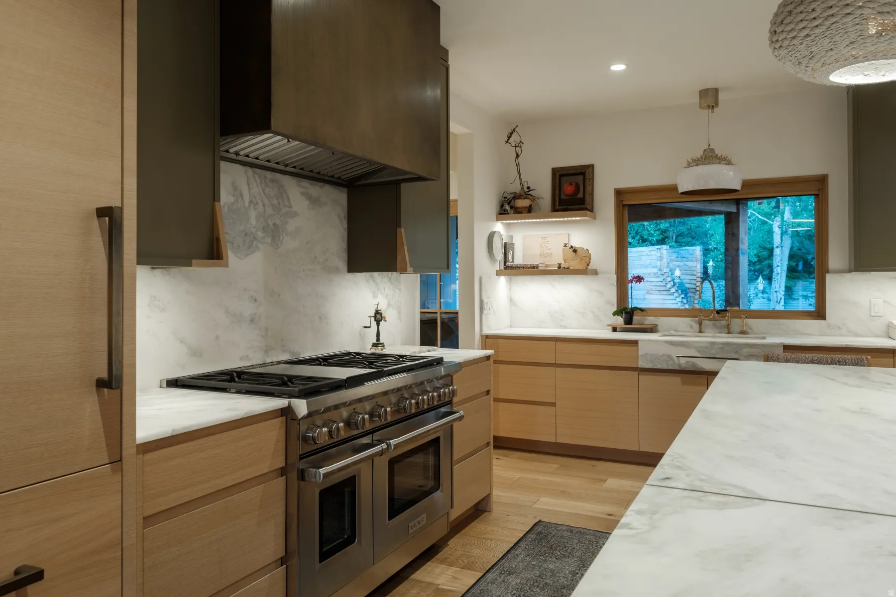 Gourmet kitchen featuring a professional-grade stainless steel range, custom range hood, stone countertops, light wood-finish cabinetry, and a built-in farmhouse sink