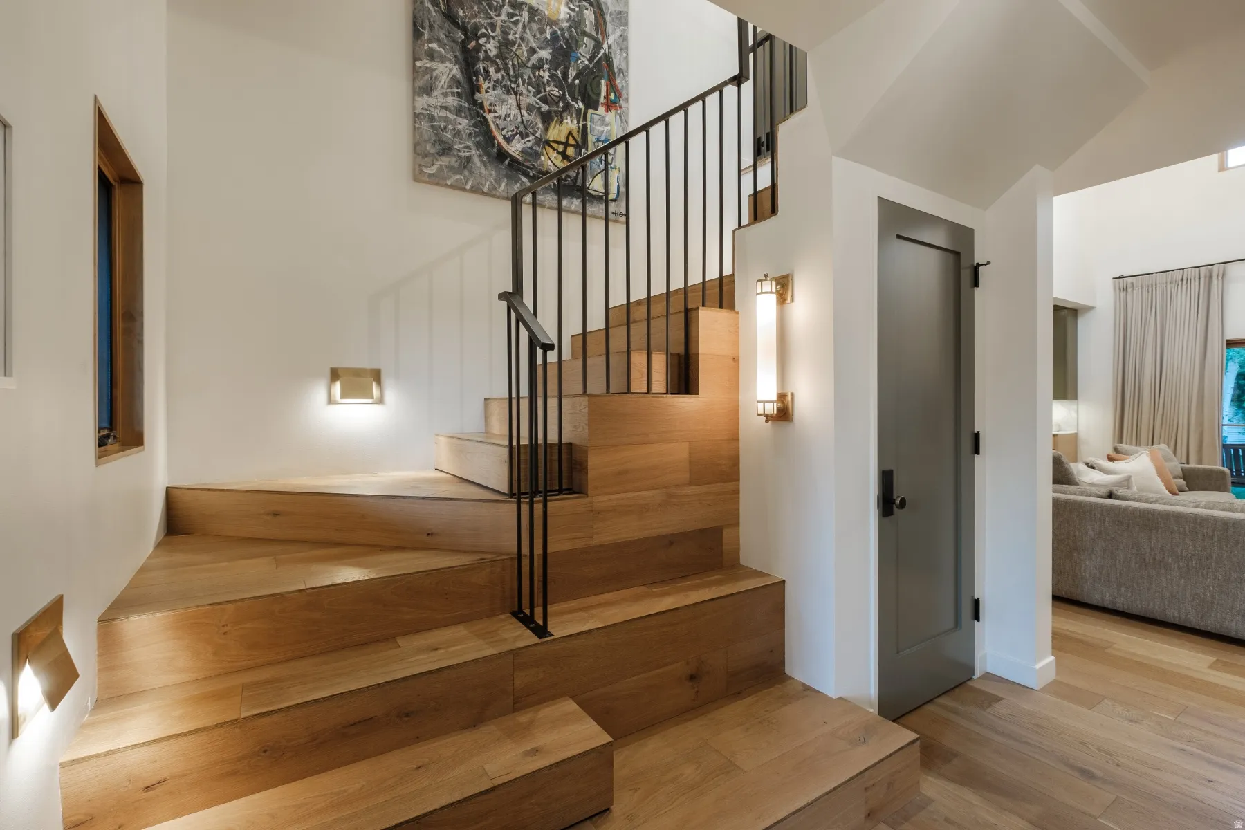 Hardwood staircase featuring an iron railing, recessed wall lighting, and a modern sconce