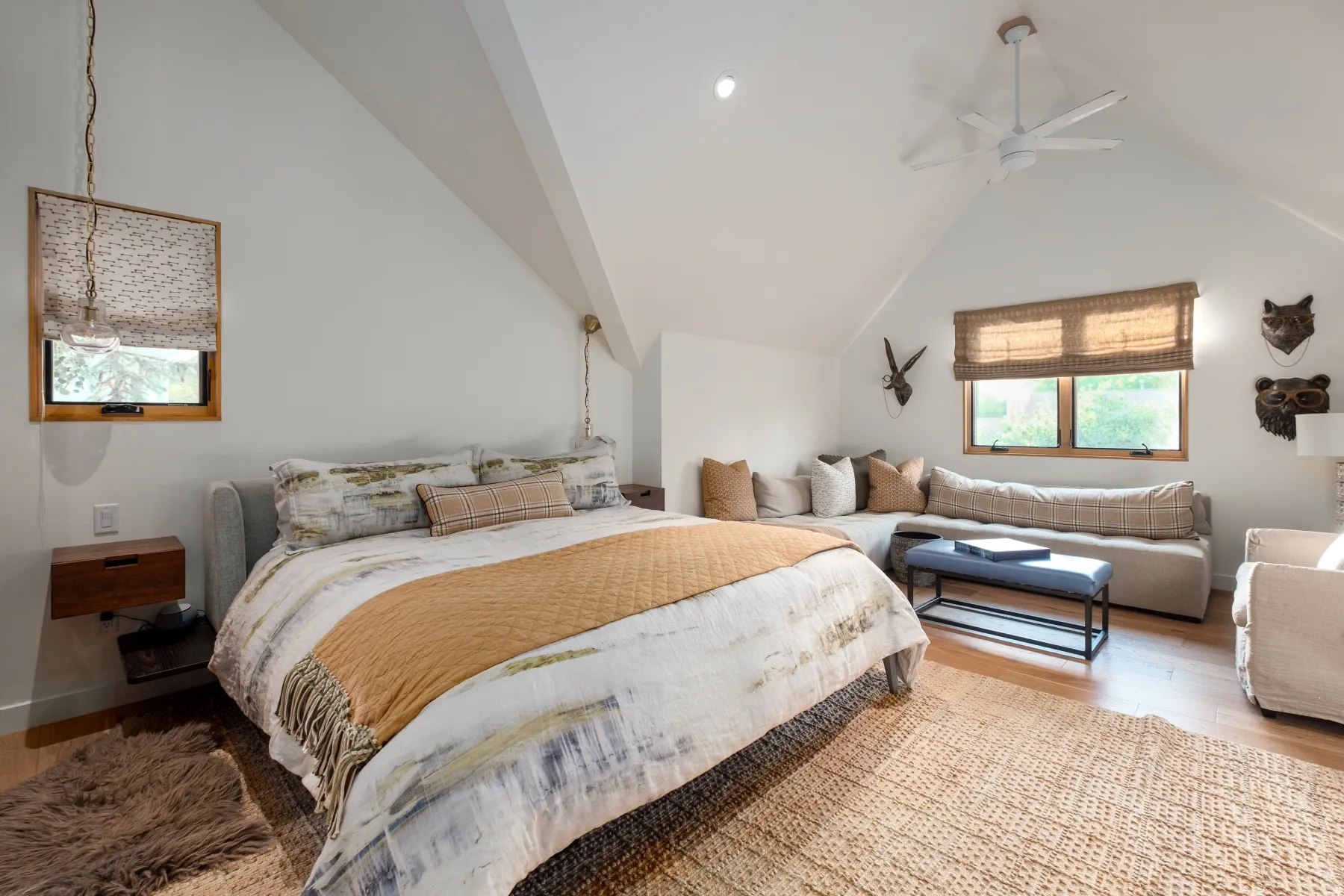 Vaulted ceiling with an integrated ceiling fan, wood-finish flooring, two large windows, two smaller windows, and built-in floating nightstands