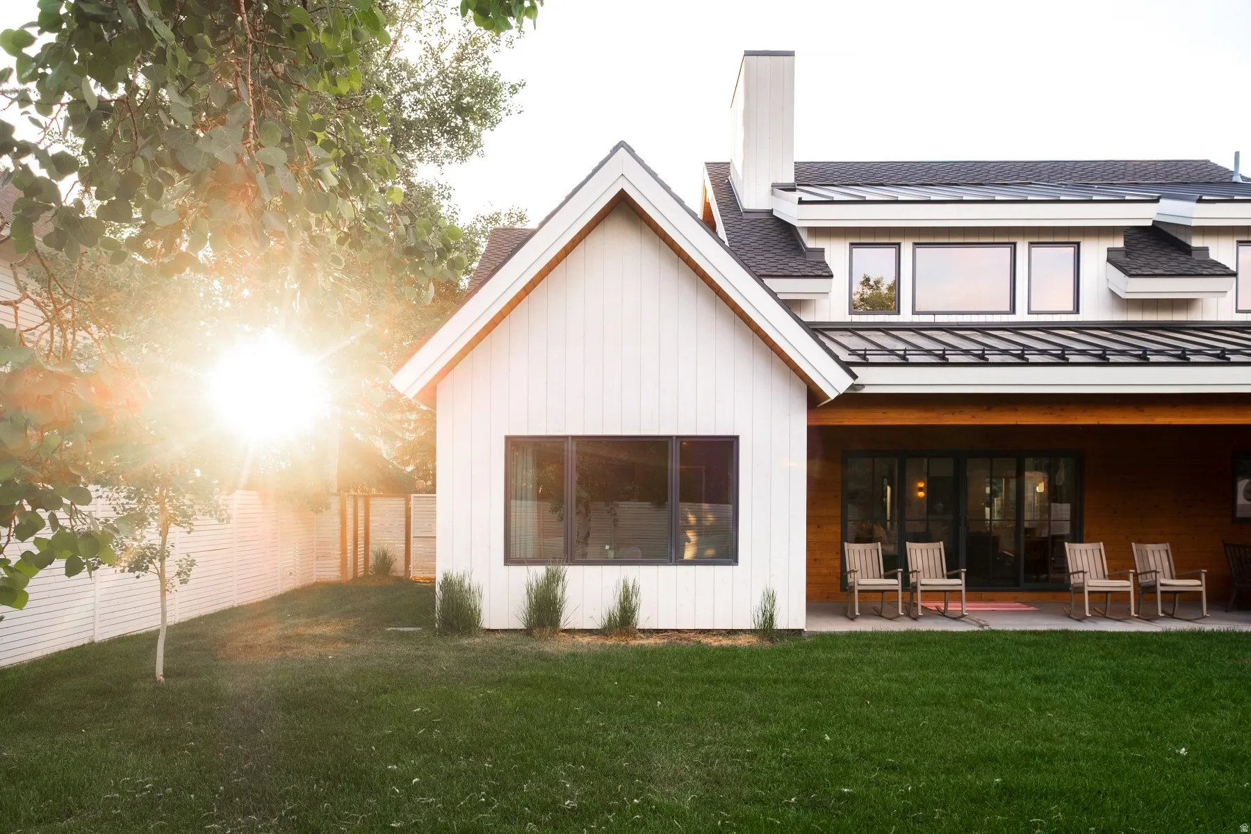 Modern white exterior with board and batten siding, black-framed windows, and a metal roof accent