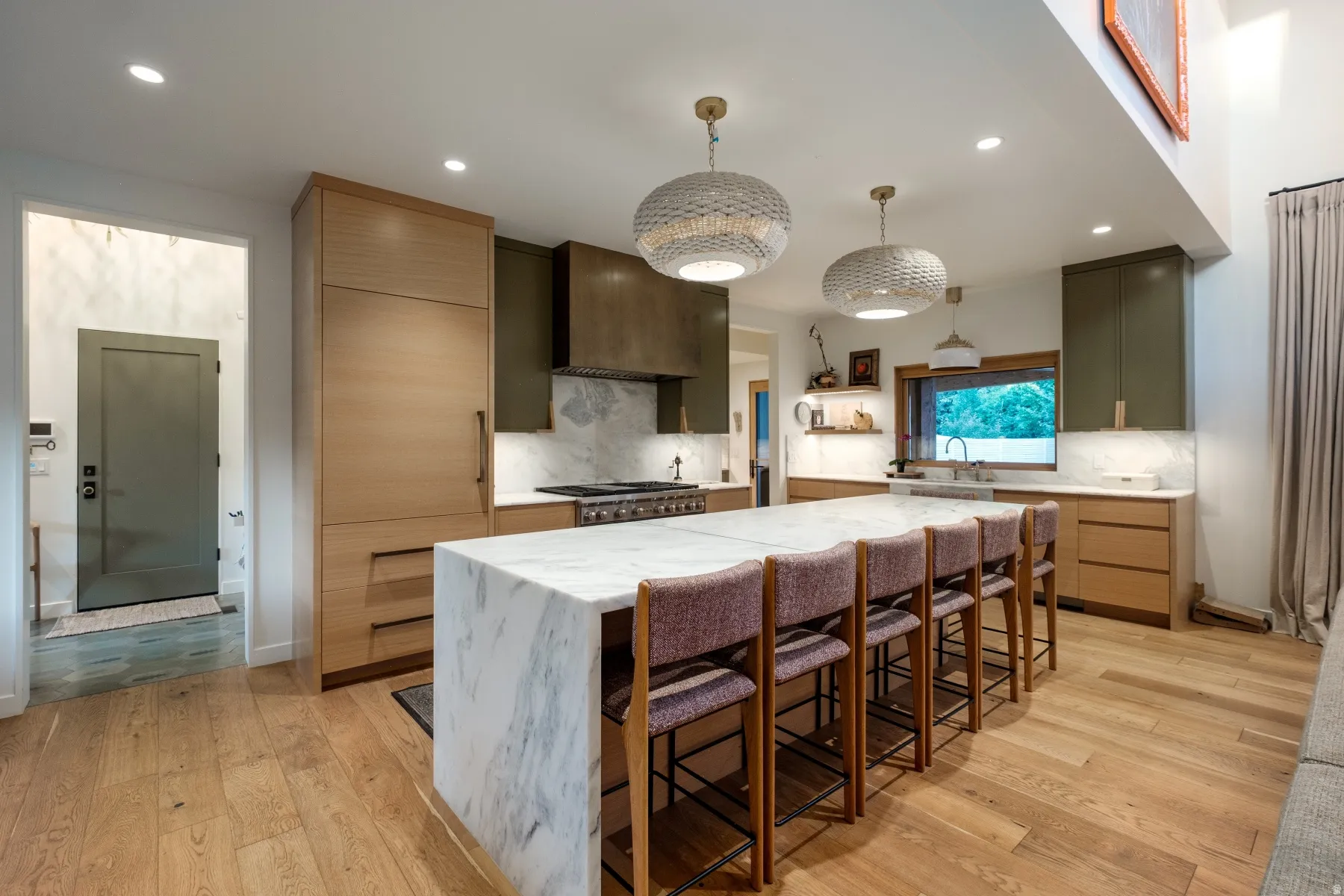 Contemporary kitchen featuring a large waterfall island with seating, panel-front appliances, wood-finish flooring, and recessed lighting