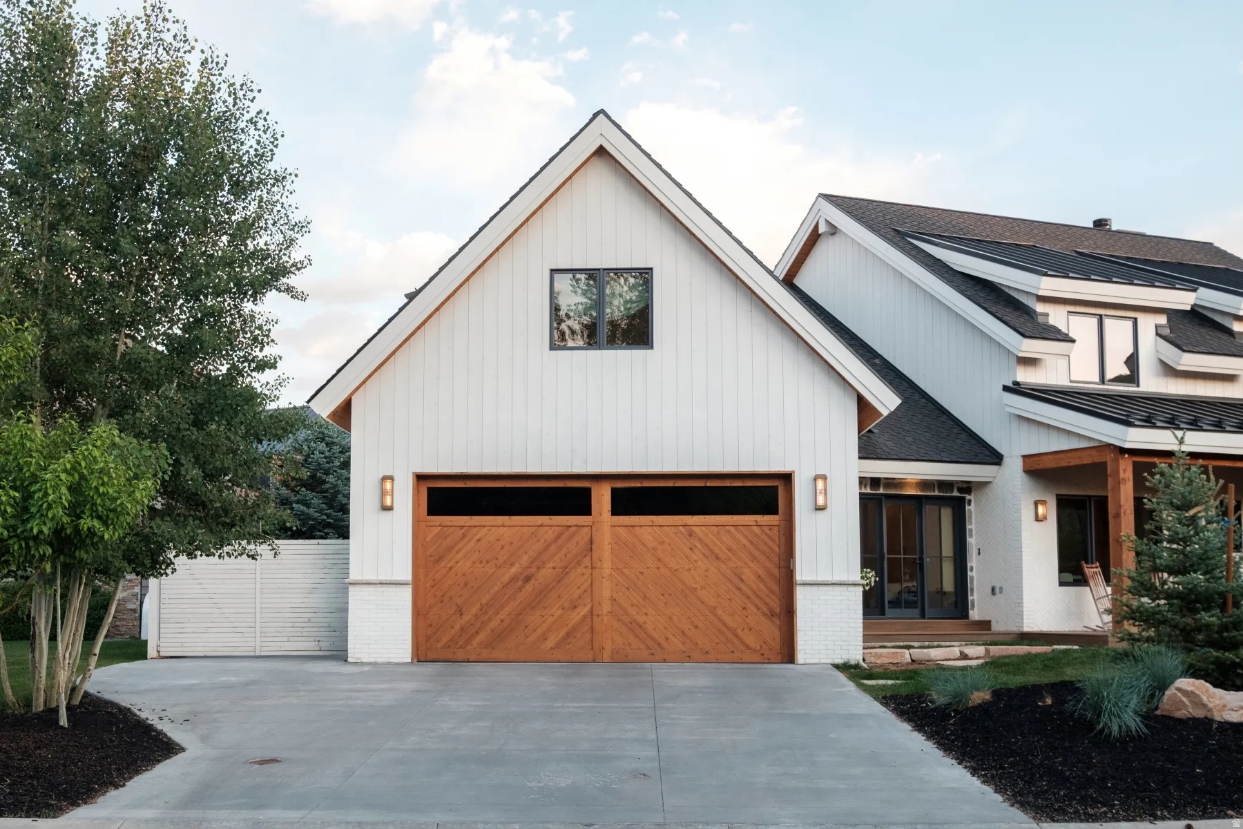 Contemporary home exterior featuring board and batten siding, a prominent wood-finish garage door, and a black shingle roof