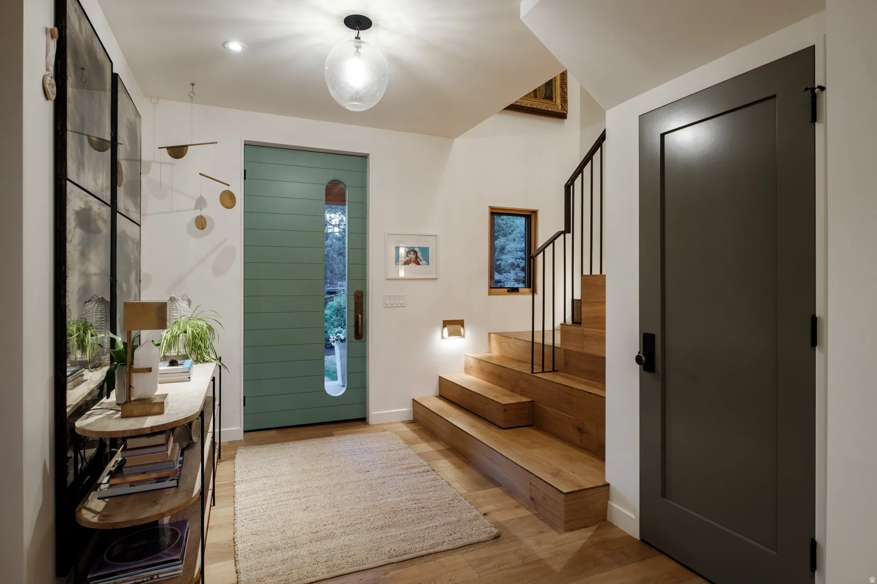 Entryway featuring a distinctive green horizontal-slat door with an elongated oval window, wood-finish flooring, and a modern staircase with black iron railings