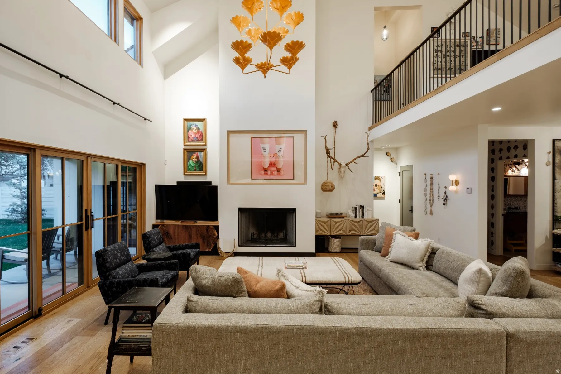Two-story living area featuring a prominent fireplace, high vaulted ceilings, hardwood flooring, and a second-story interior balcony with black metal railing