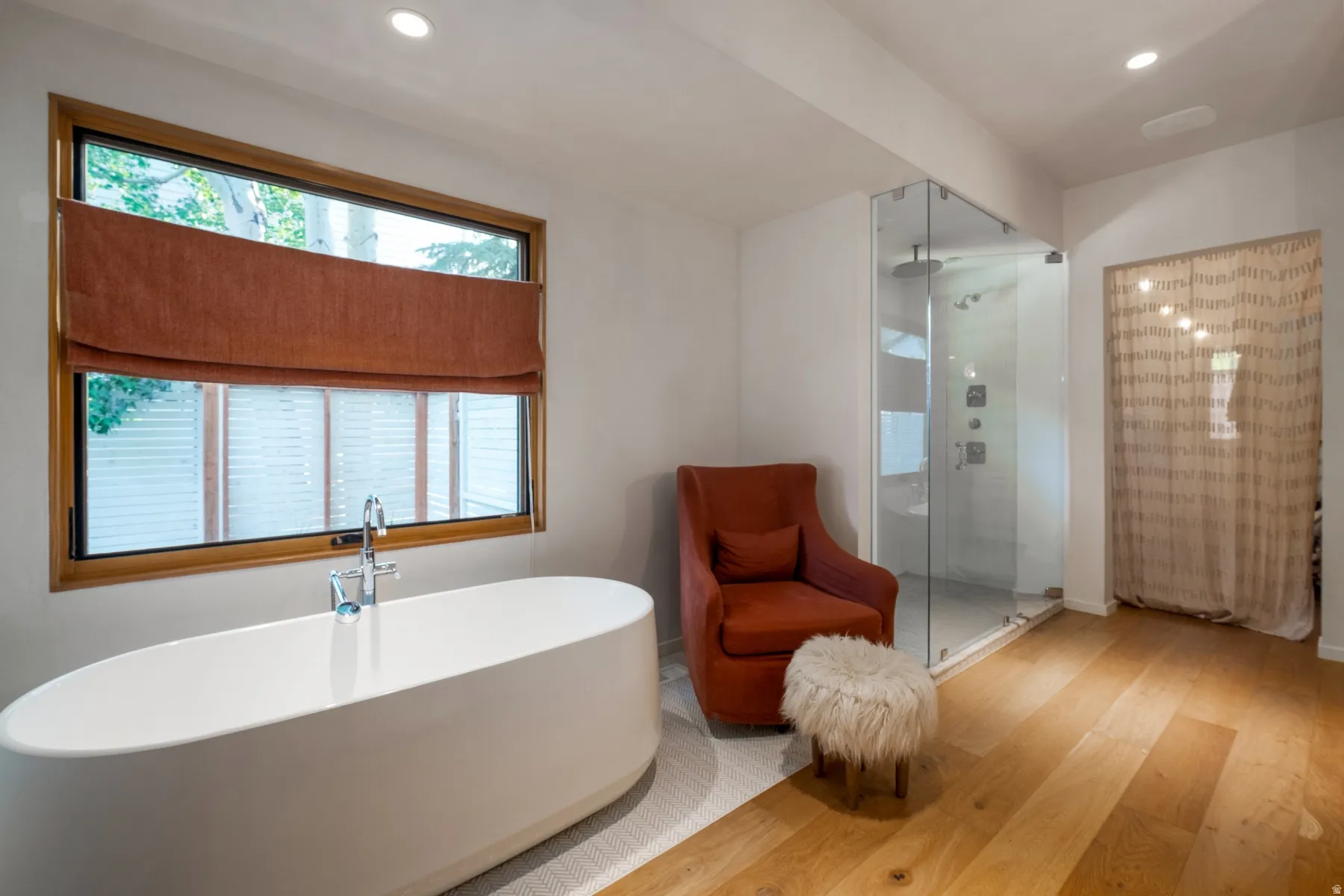 Bathroom featuring a freestanding soaking tub, a frameless glass shower enclosure with multiple shower heads, and wood-finish flooring