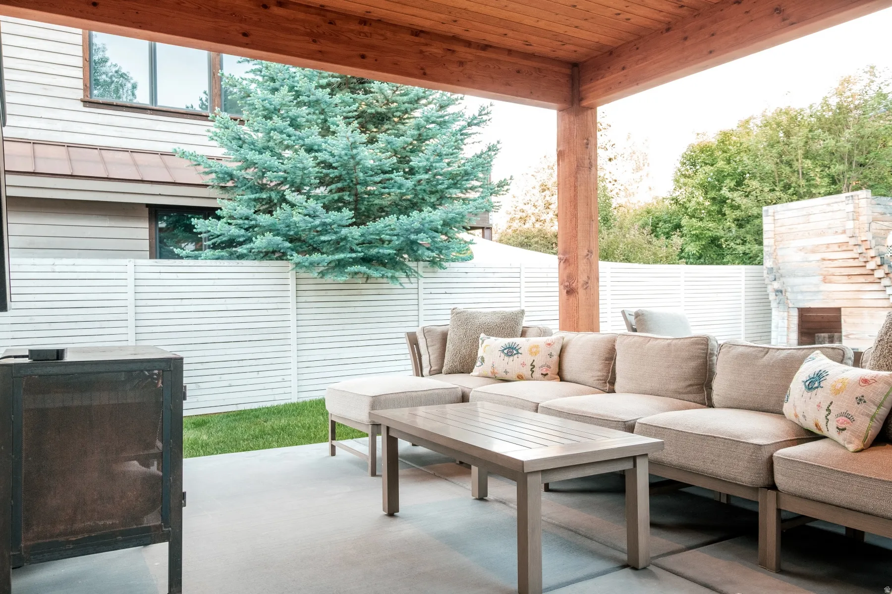 Covered outdoor patio featuring a wooden ceiling, concrete flooring, and a stone fireplace structure