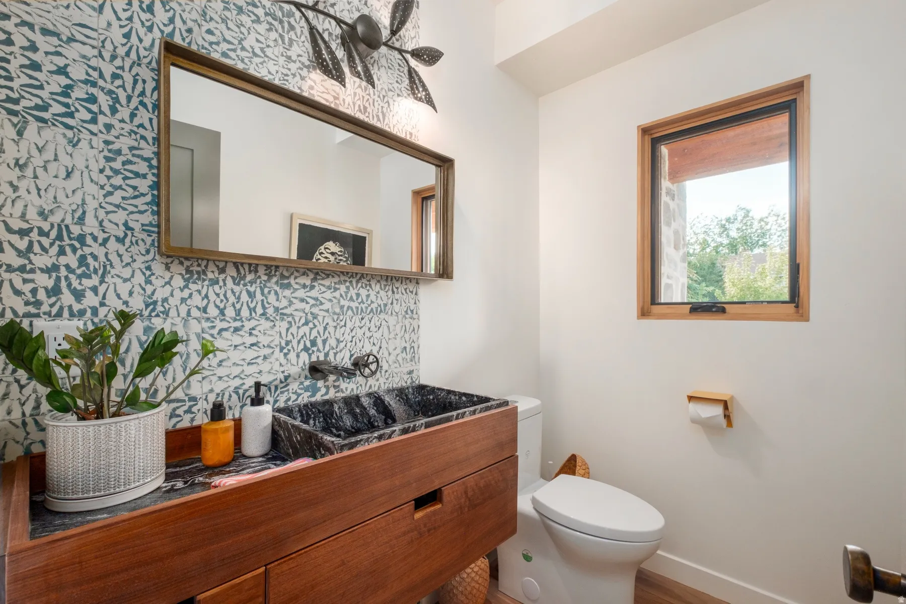 Vanity area featuring a wall-mounted rectangular mirror, black stone vessel sink, and a wood-finish vanity with storage