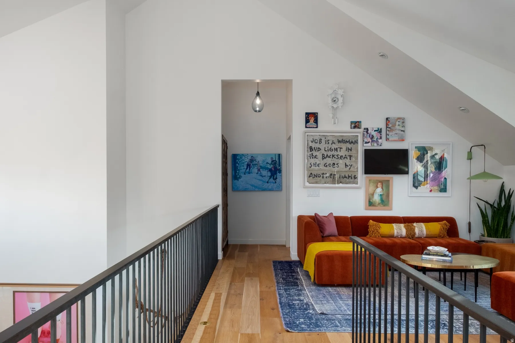 Upper-level landing featuring wood-finish flooring, a contemporary black metal railing, and a vaulted ceiling