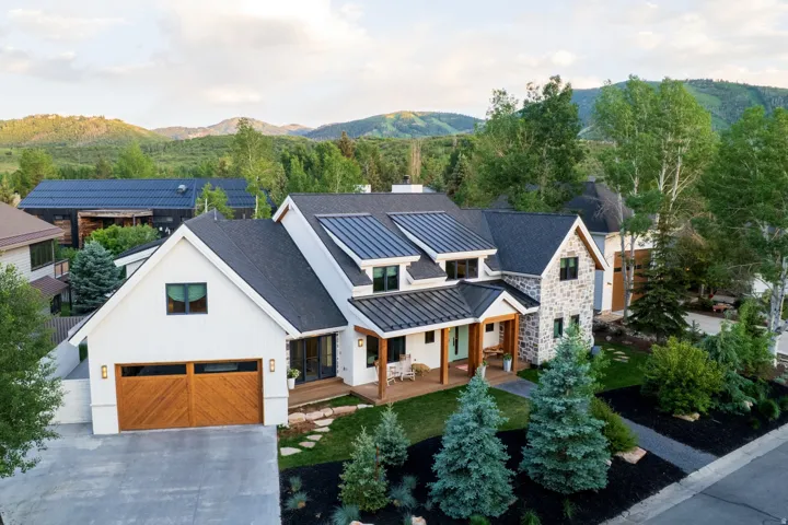 Modern farmhouse exterior featuring white board and batten siding, natural stone accents, and a dark shingle roof with metal roof details