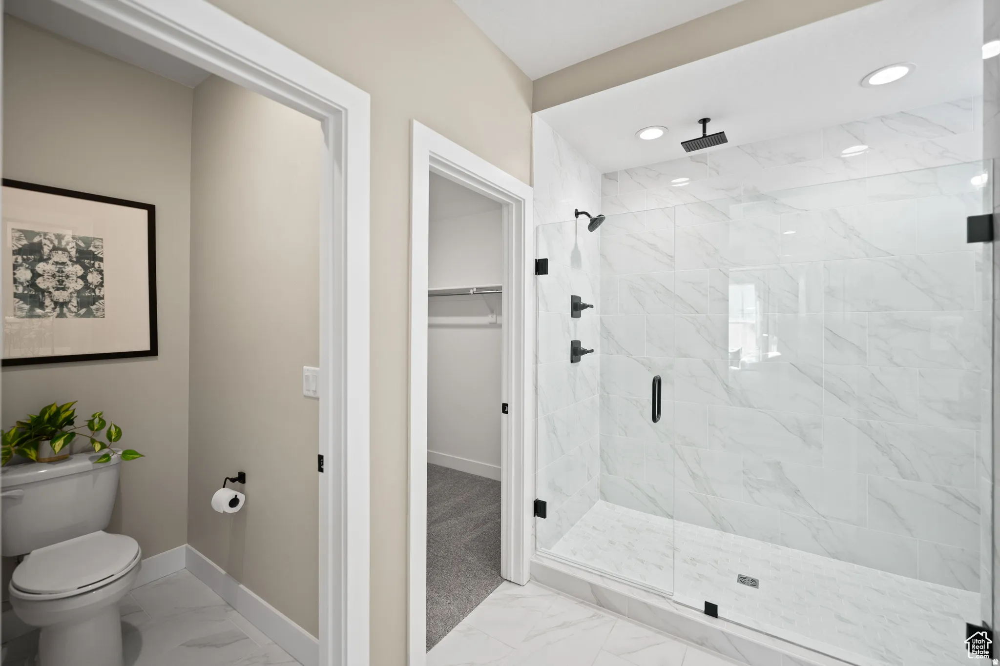 Spacious bathroom featuring a frameless glass shower enclosure with matte black hardware, a rainfall showerhead, and white marble-look tile