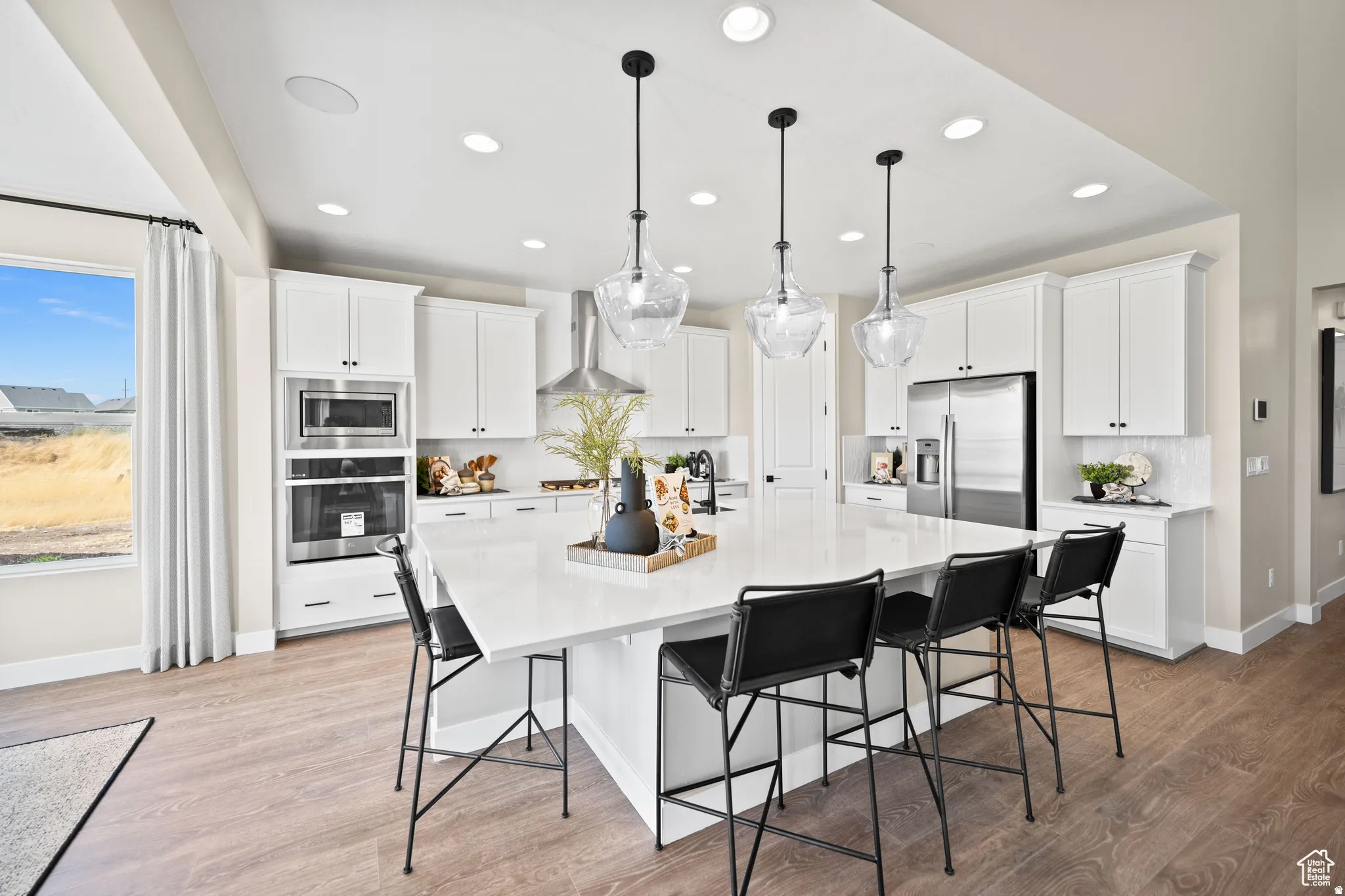 Spacious kitchen featuring an oversized island with seating, white shaker cabinetry, stainless steel appliances, and wood-finish flooring