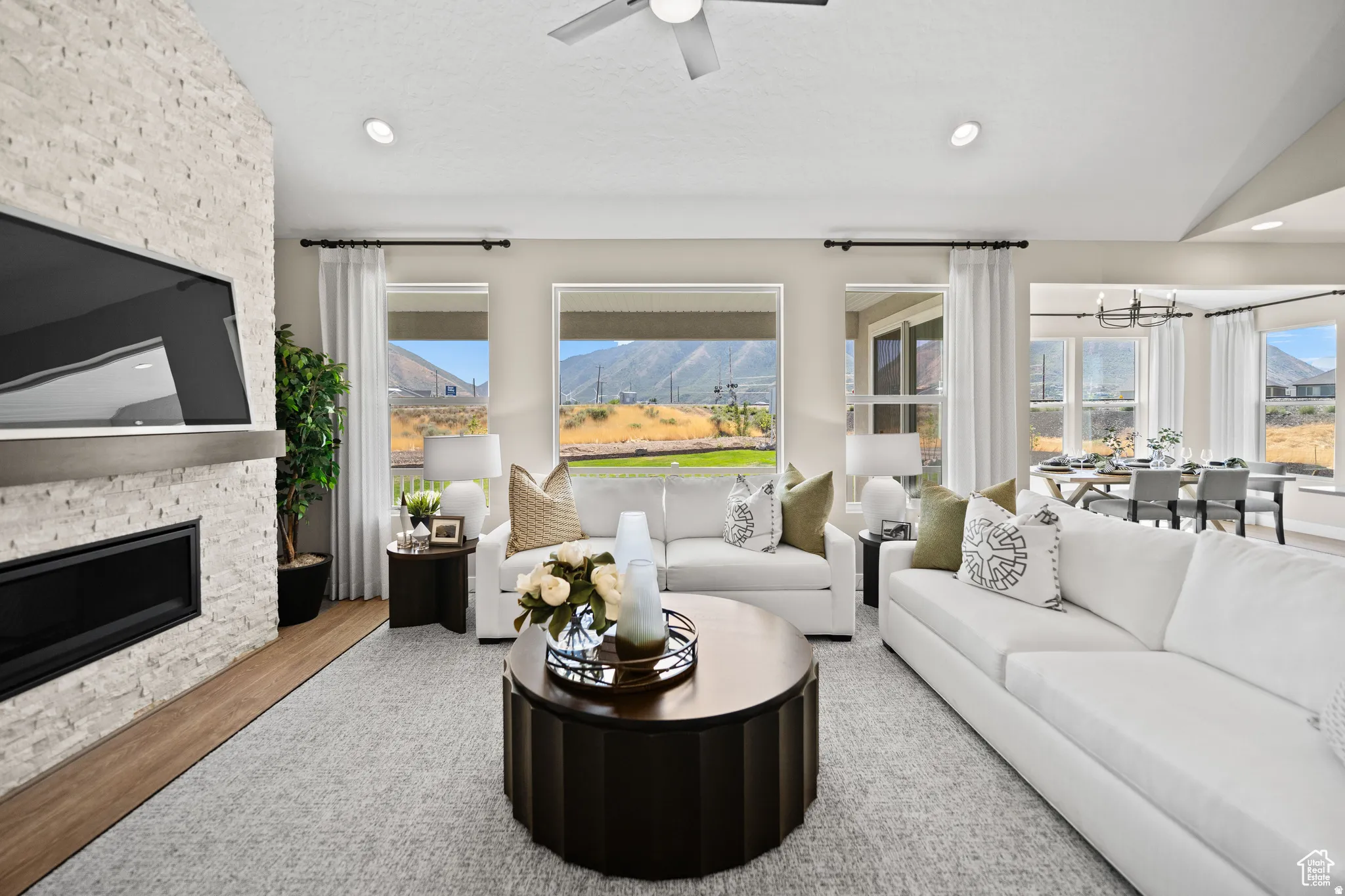 Expansive living area featuring a stacked stone fireplace with a floating mantel, large windows with mountain scenery, recessed lighting, and wood-finish flooring