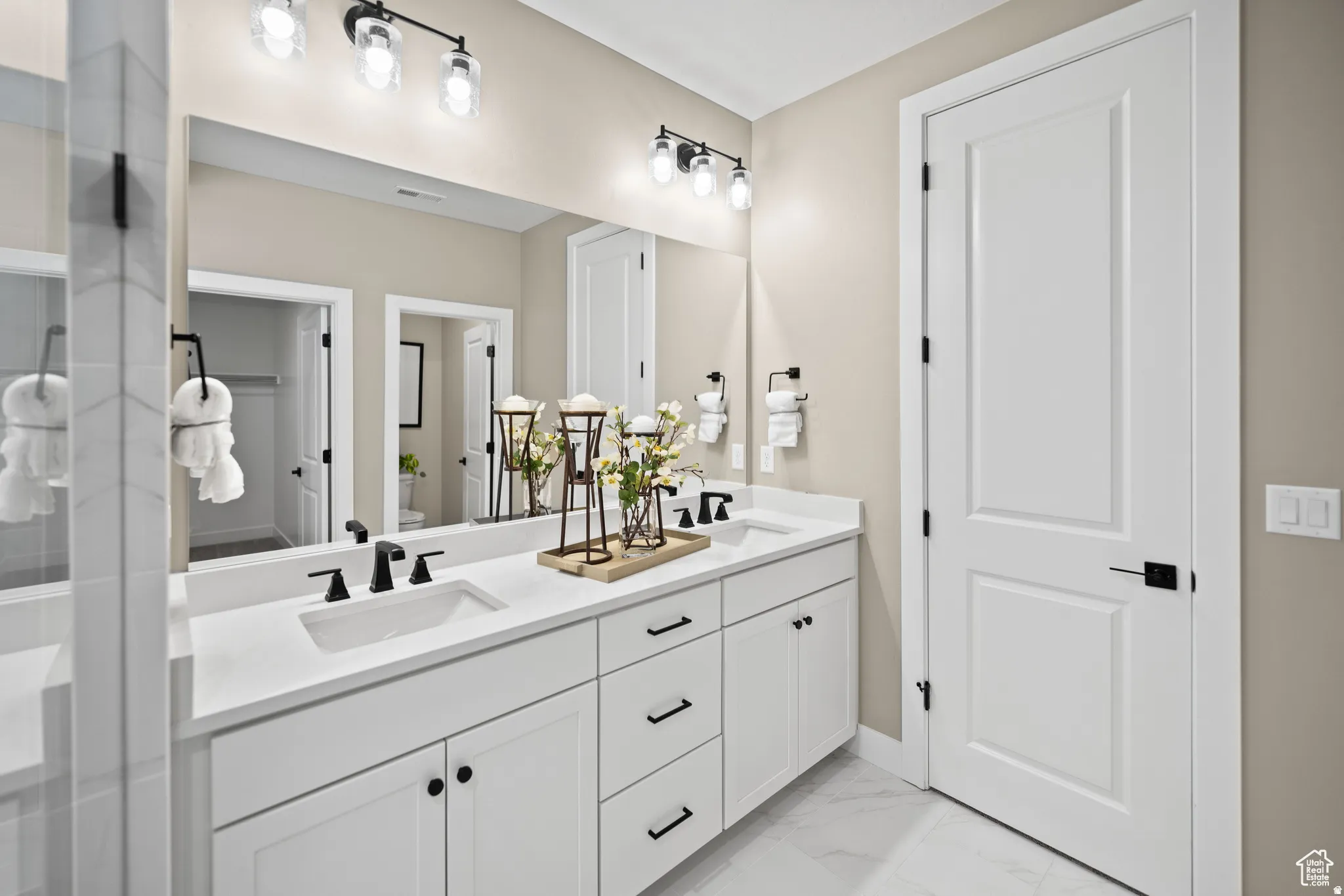 Double vanity featuring two undermount sinks, white cabinetry with black hardware, and an expansive mirror