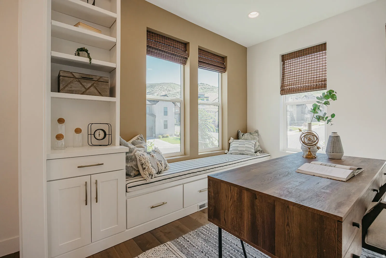 Integrated window seat with built-in storage drawers, bordered by multiple windows with woven Roman shades